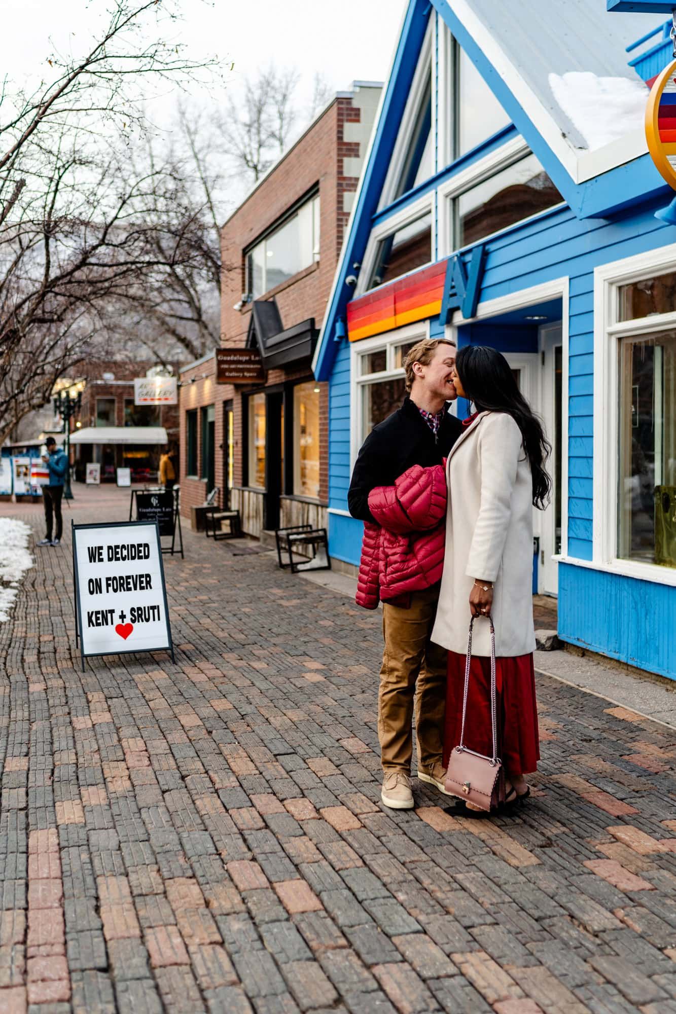 A couple sharing an intimate moment outside a colorful blue building on a brick sidewalk.
