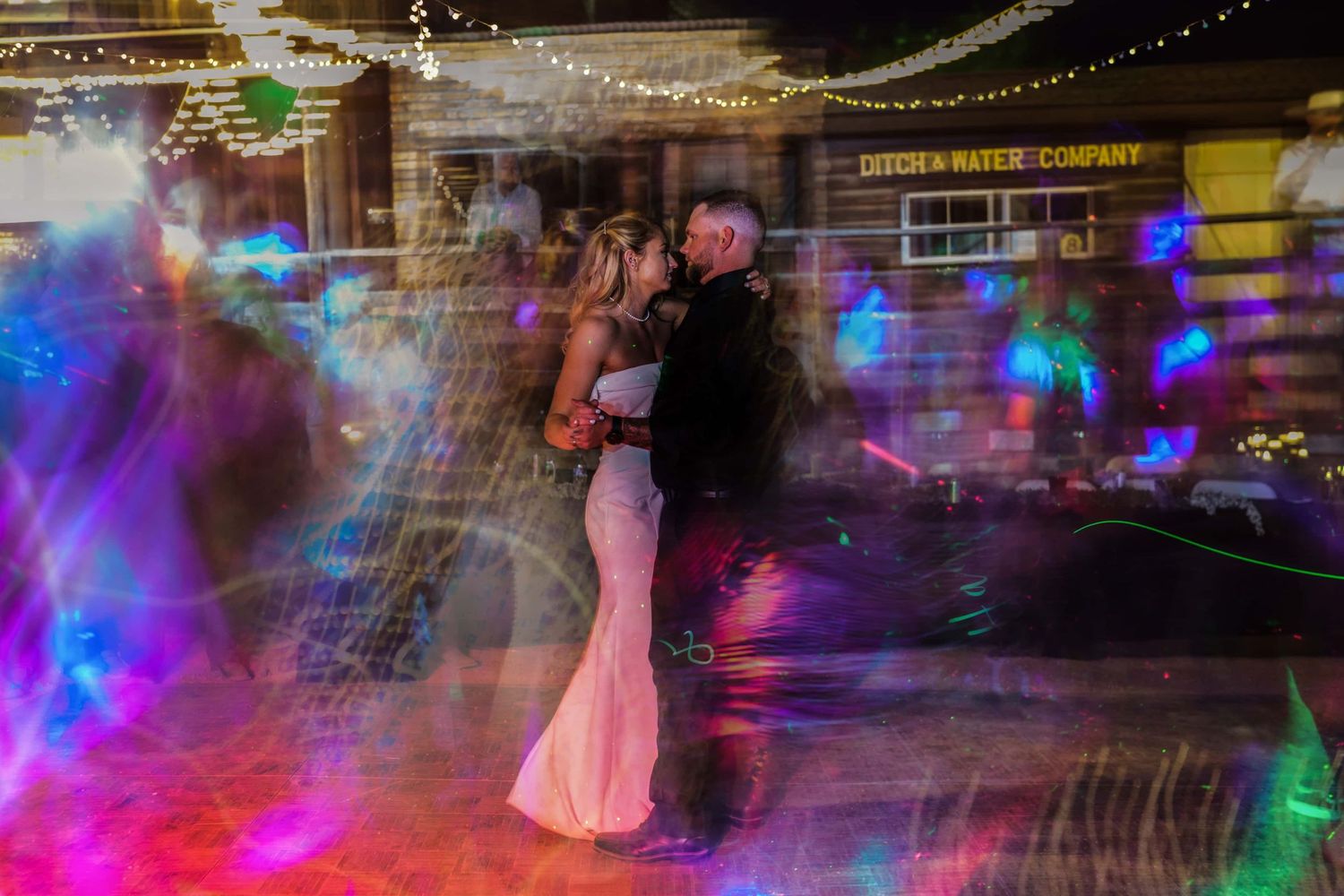 A couple dancing at their wedding reception surrounded by colorful lights and long exposure effects.
