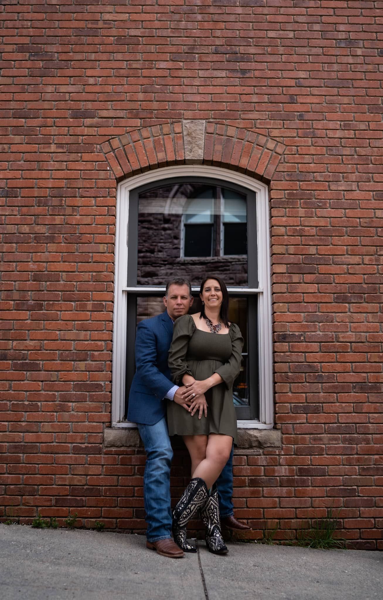 Couple posing in front of arched brick window in urban setting.