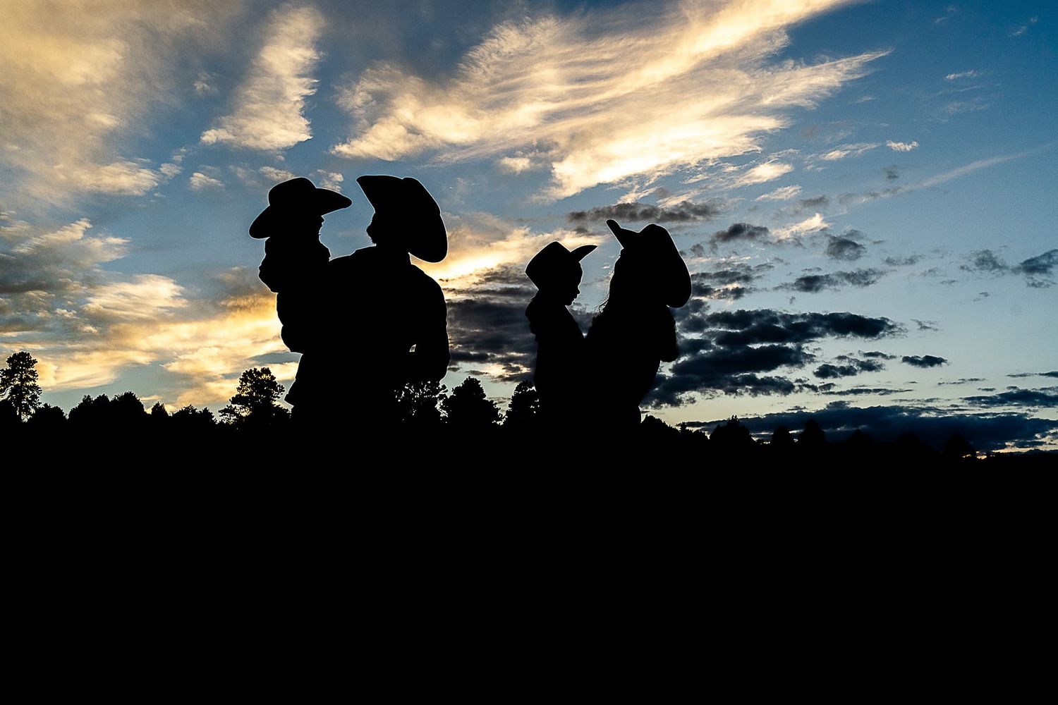Silhouettes of cowboy figures against dramatic sunset sky.