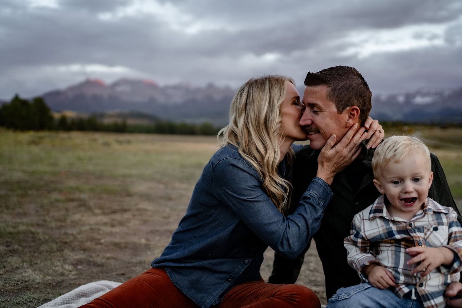 Intimate family moment captured against backdrop of mountain landscape at dusk.