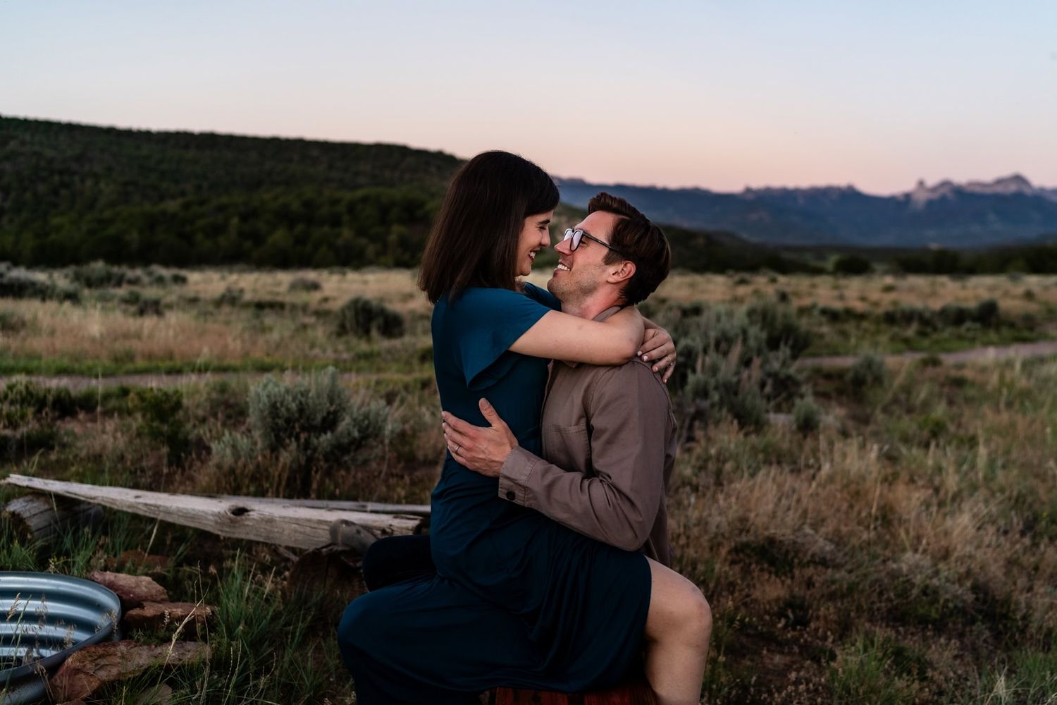 A romantic sunset embrace between a couple in an open field with mountains in the distance.