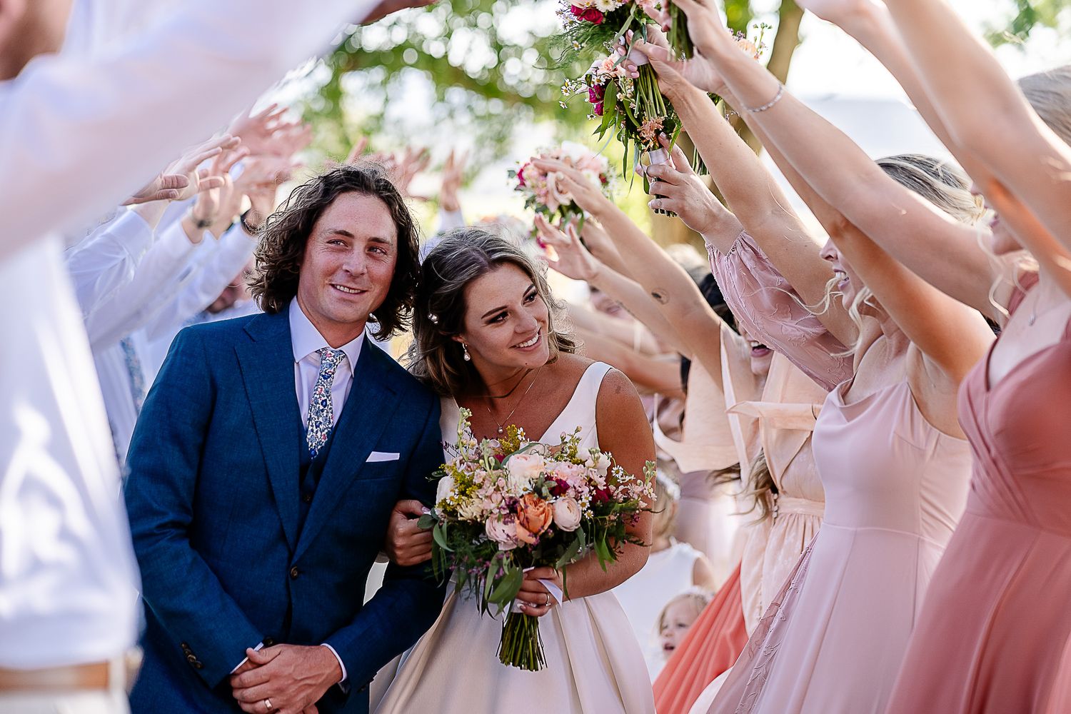 Wedding celebration with attendants in pink dresses celebrating under raised flower bouquets.