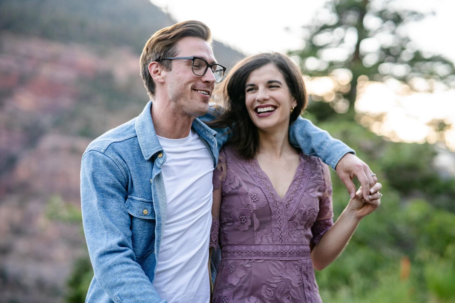 A joyful couple laughing together outdoors with red rock mountains in the background.