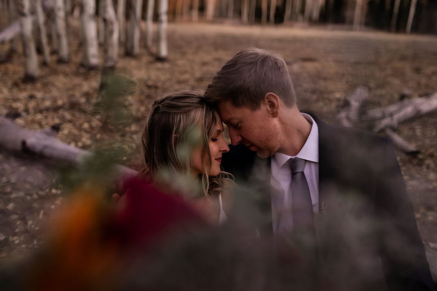 Romantic intimate moment captured through foliage in an autumn forest setting.