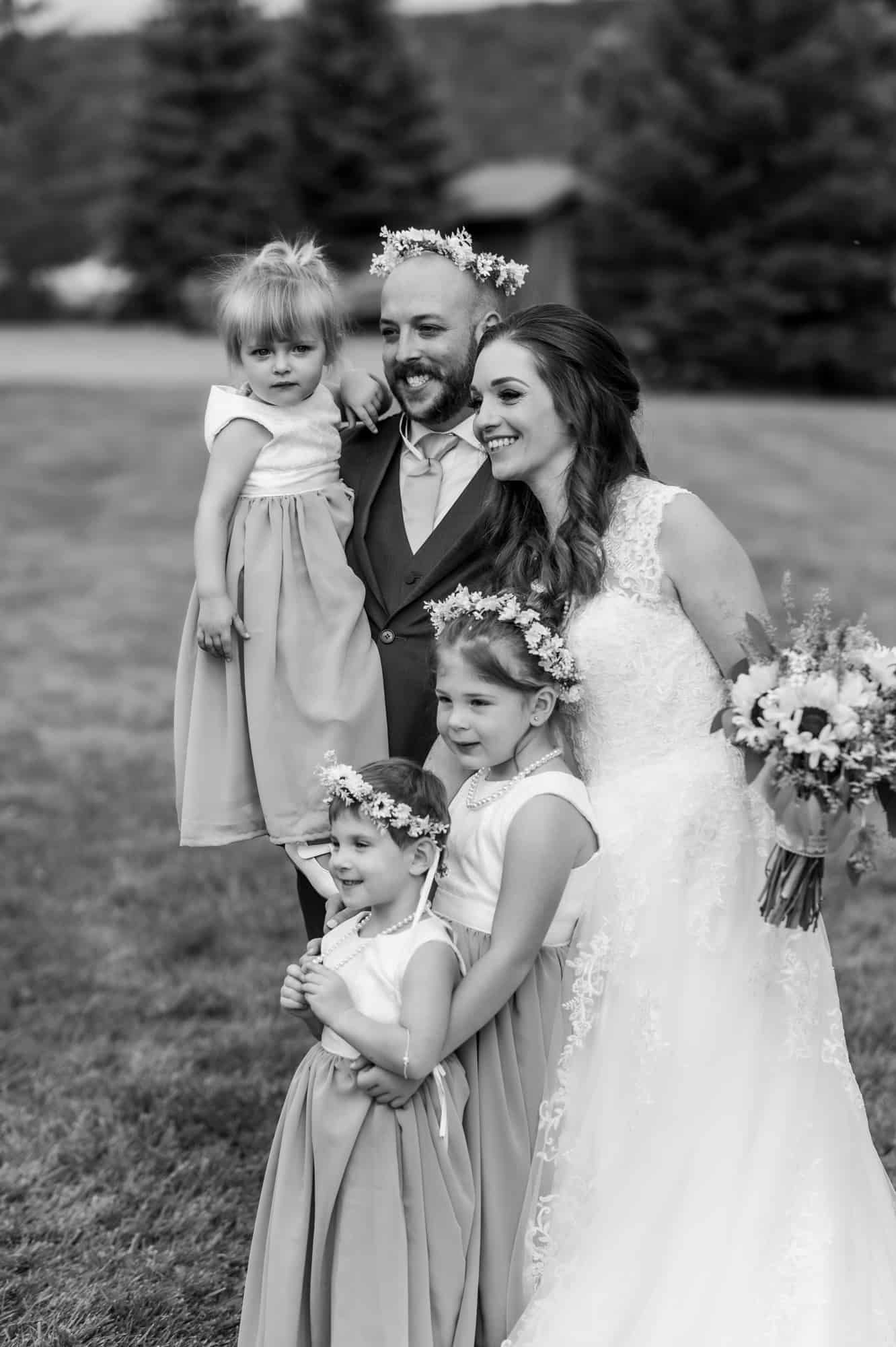 Black and white portrait of newlyweds with flower girls in matching dresses on a grassy hill at one of the best Montrose wedding venues