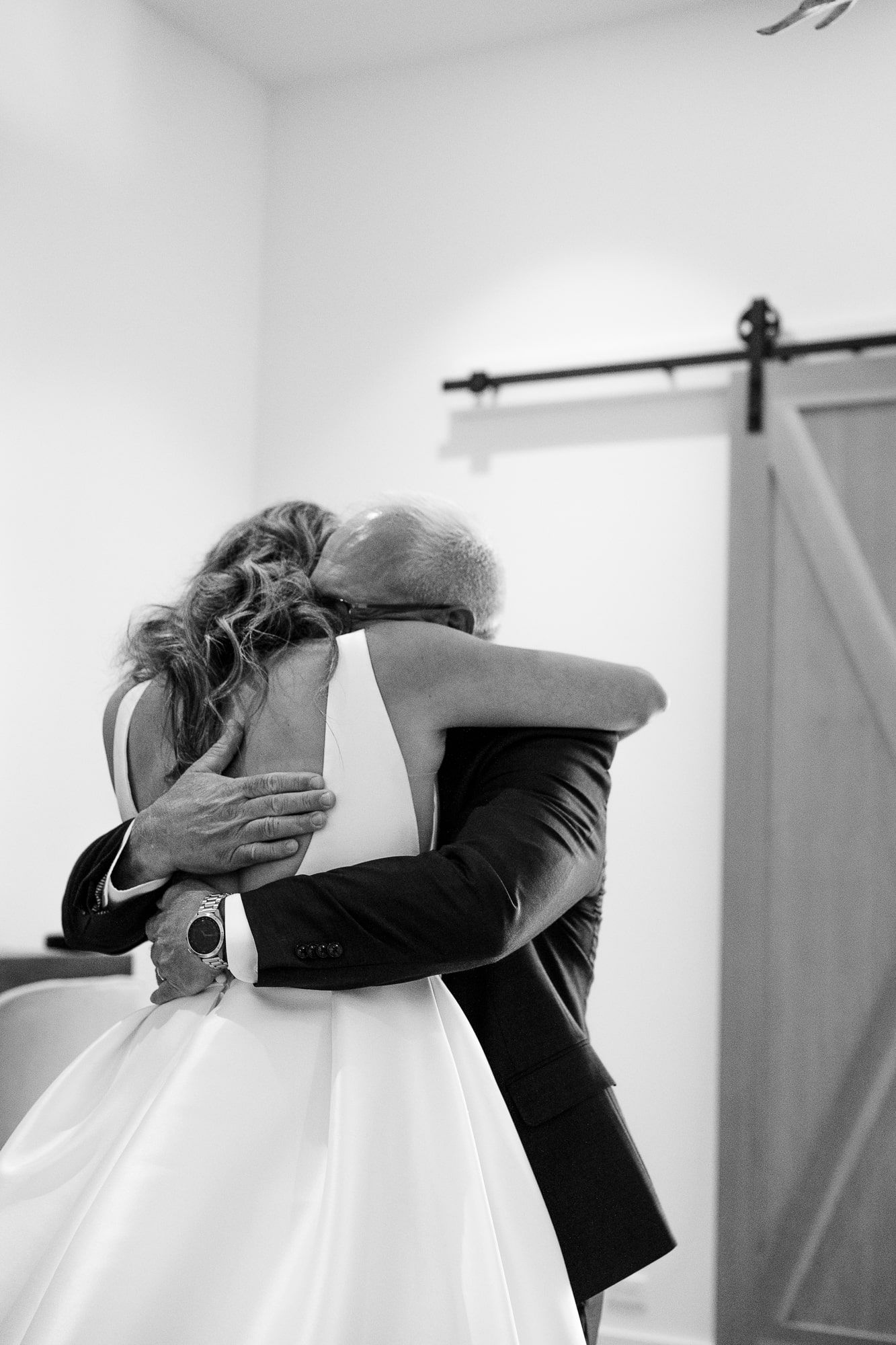 Emotional embrace captured in black and white with flowing wedding dress. Image was taken at rustic barn venue near Montrose Colorado.