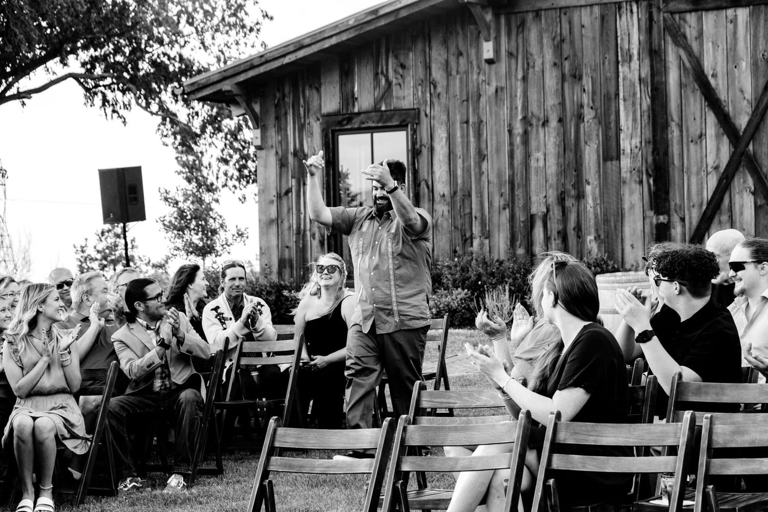 Black and white photo of outdoor wedding ceremony with rustic barn venue near Montrose Colorado as the backdrop.