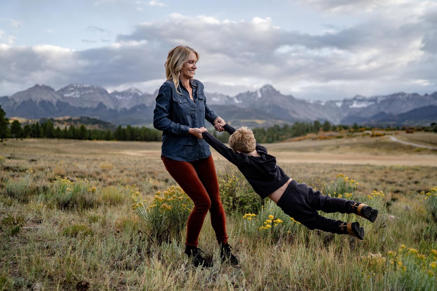Playful moment in a mountain meadow with dramatic snow-capped peaks in the background.