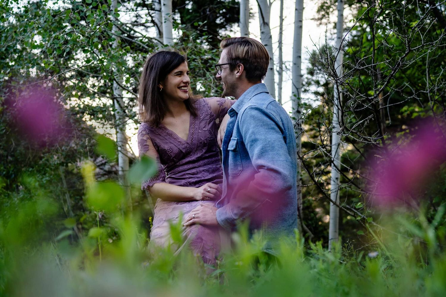 A romantic couple embracing in nature with green foliage surrounding them.