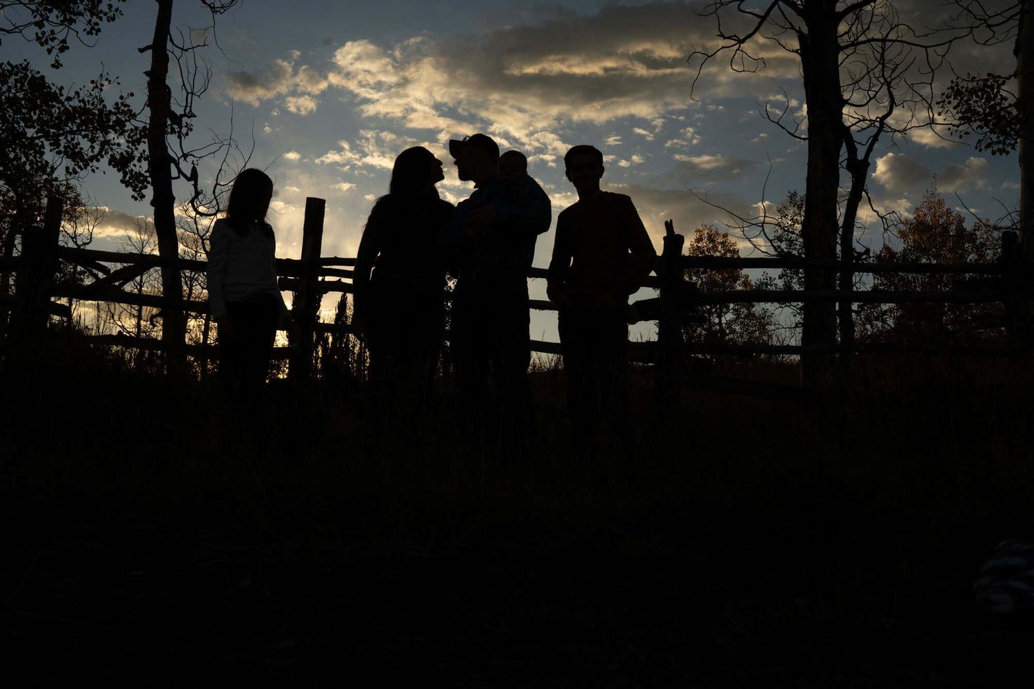 Silhouettes of people against dramatic sunset sky leaning on fence.