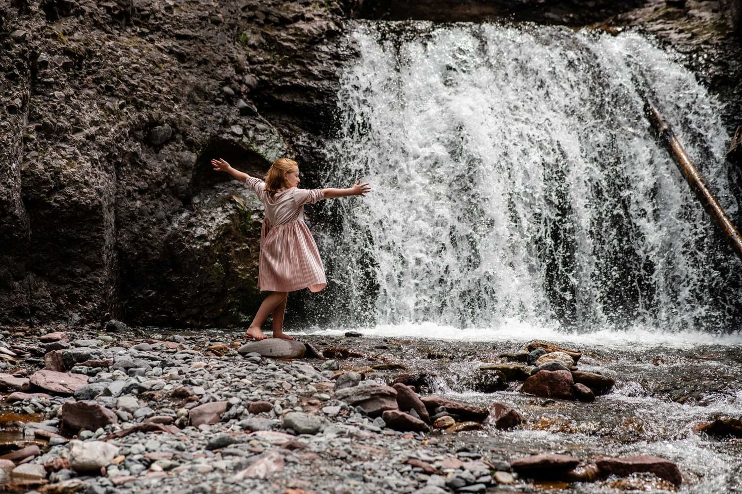 Person in pink dress twirling joyfully in front of a cascading waterfall.