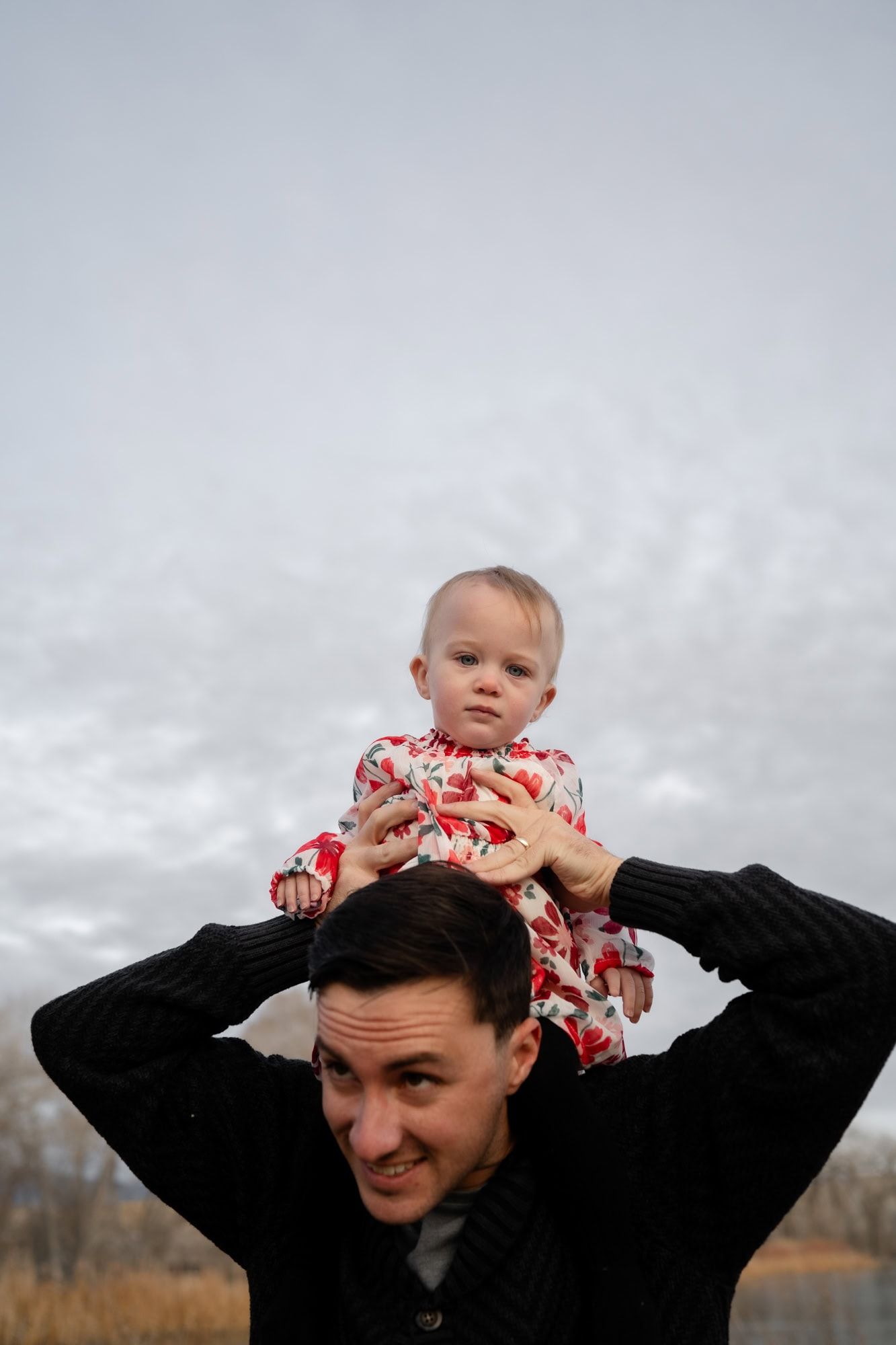 A parent gives their child a shoulder ride against a cloudy sky backdrop.