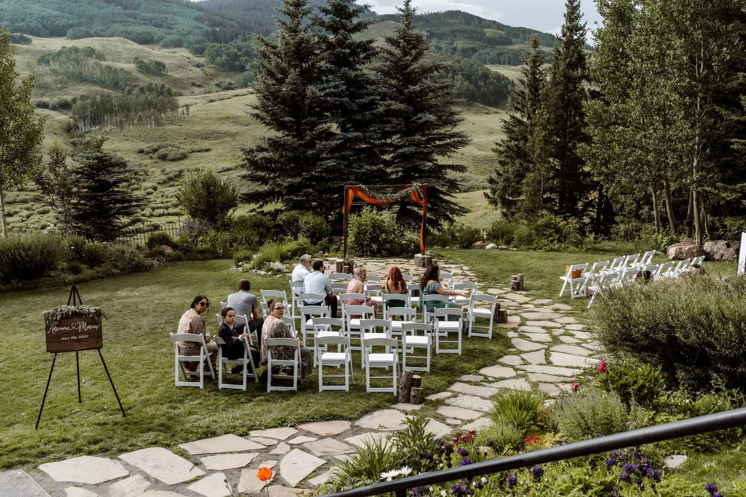 Intimate outdoor mountain wedding ceremony setup with white chairs and wooden arch surrounded by evergreen trees.