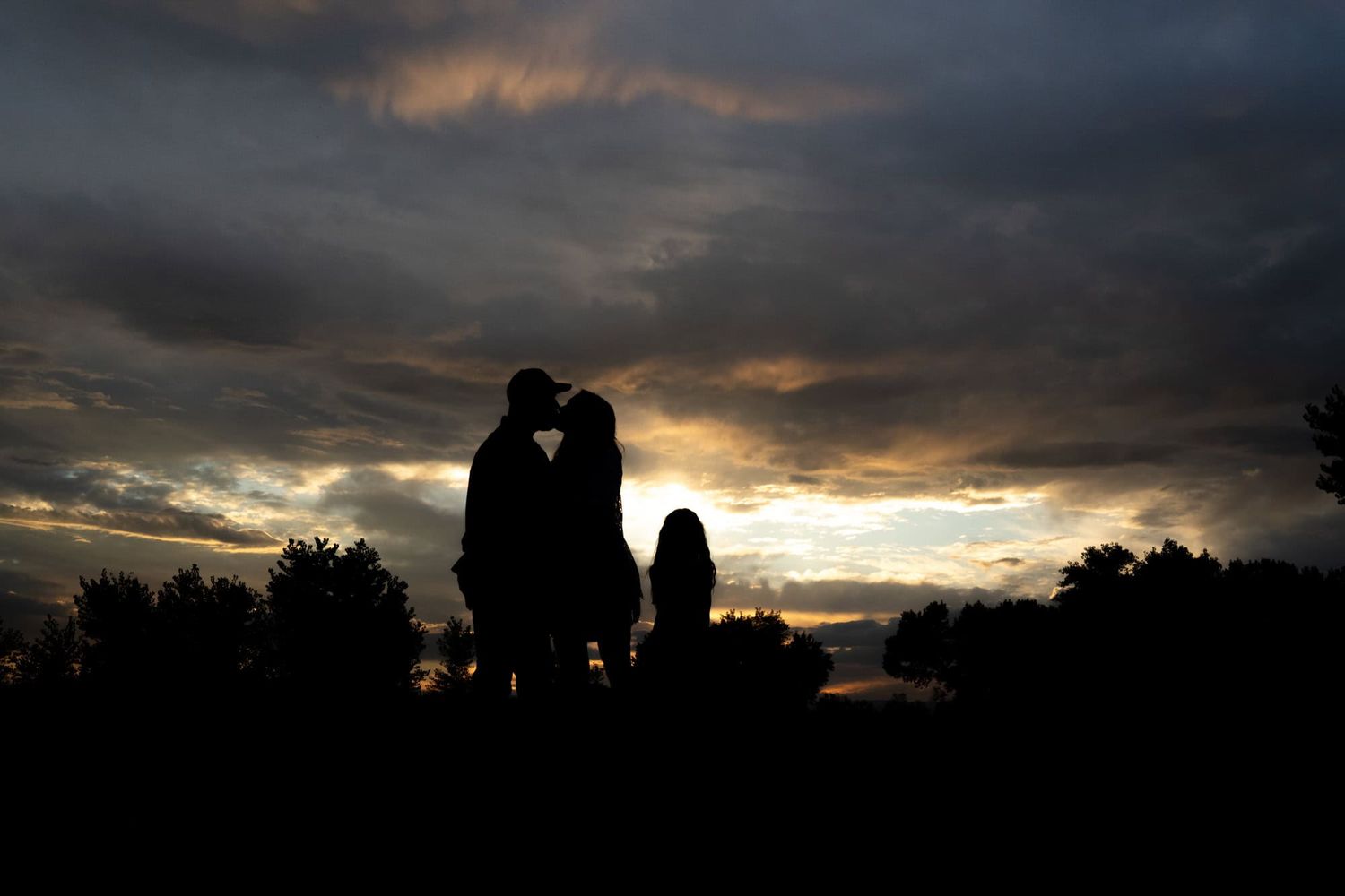 Silhouettes of people against a dramatic sunset sky with golden clouds.
