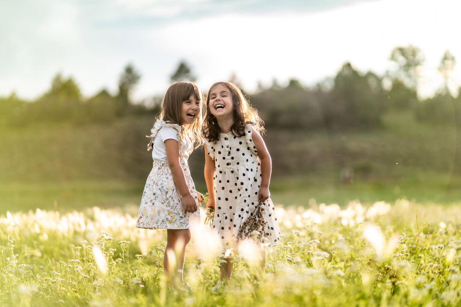 Two people sharing laughter while standing in a sun-drenched meadow of wildflowers.