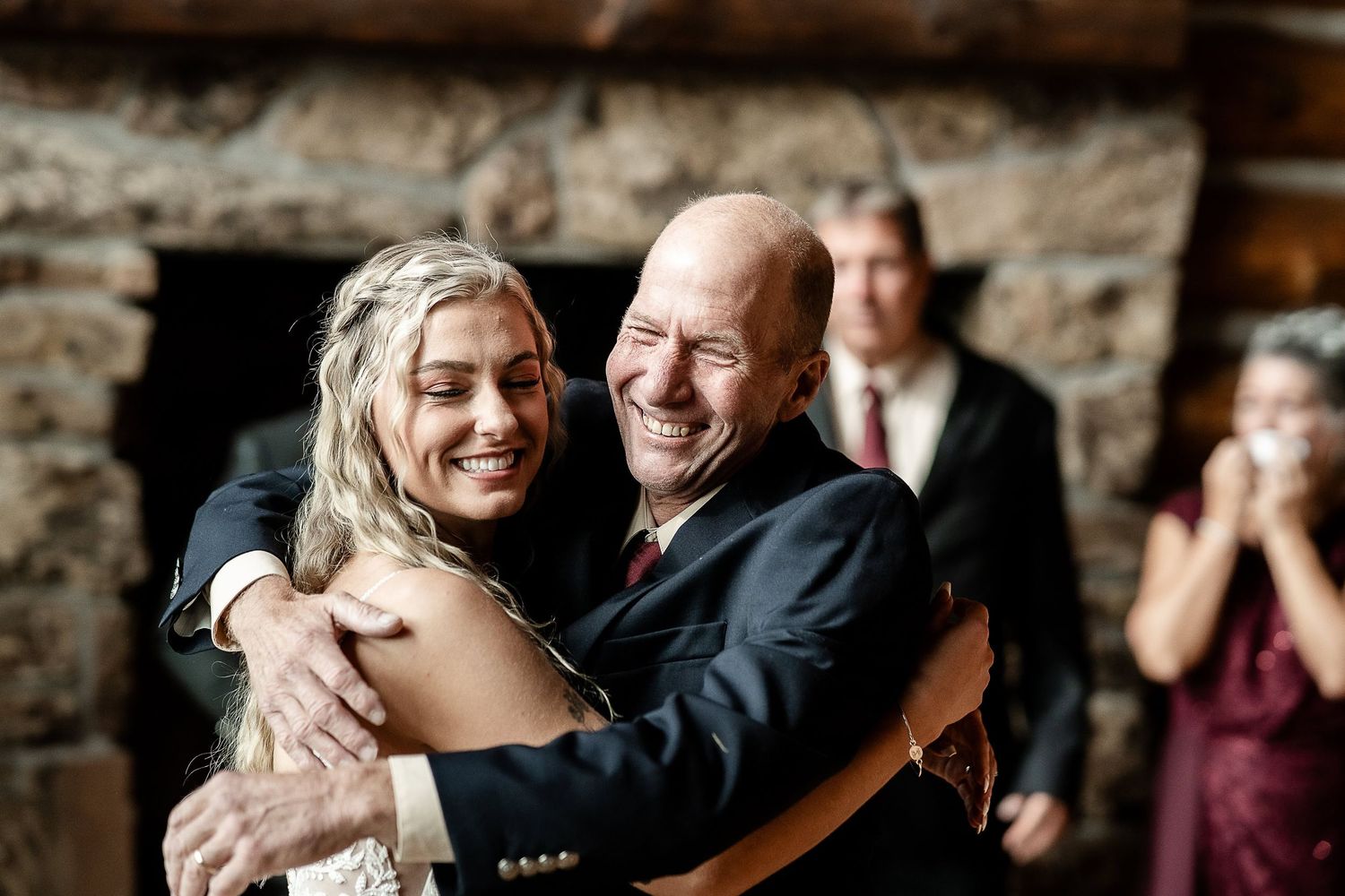 Two people share a joyful embrace during a wedding celebration while party guests watch in the background.