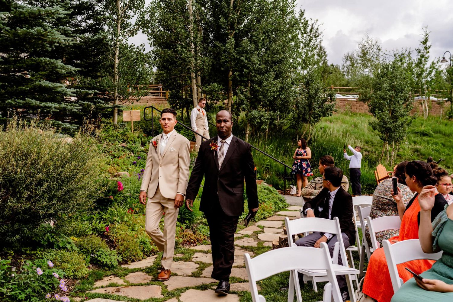 Wedding guests walking along a stone path through a mountain garden setting.