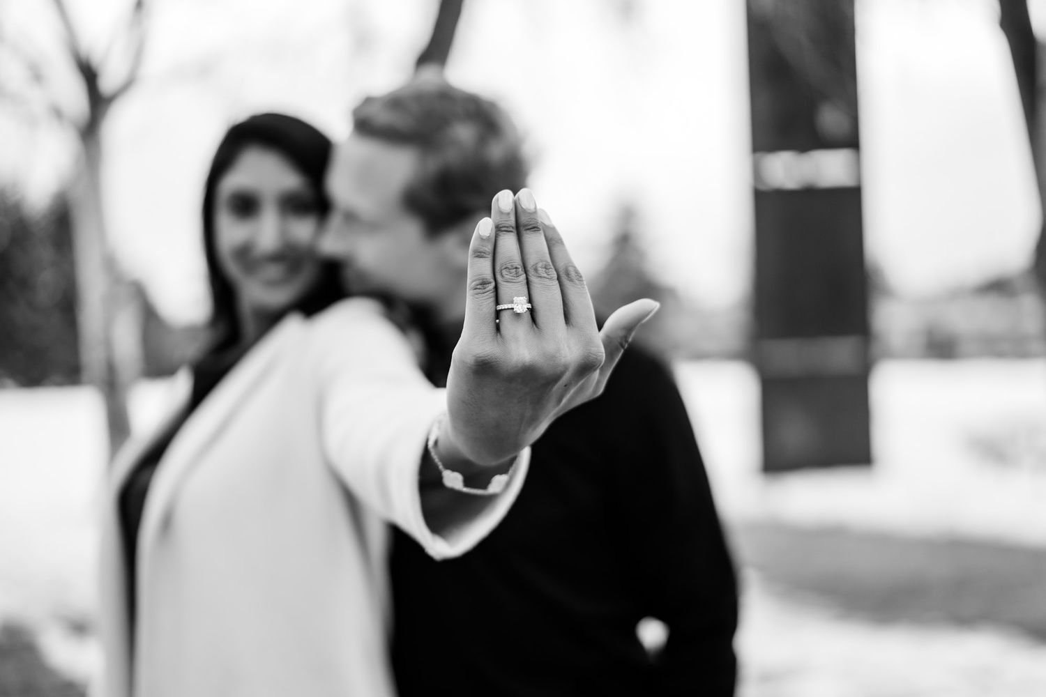 A close-up shot showcasing an engagement ring with a couple in soft focus background.