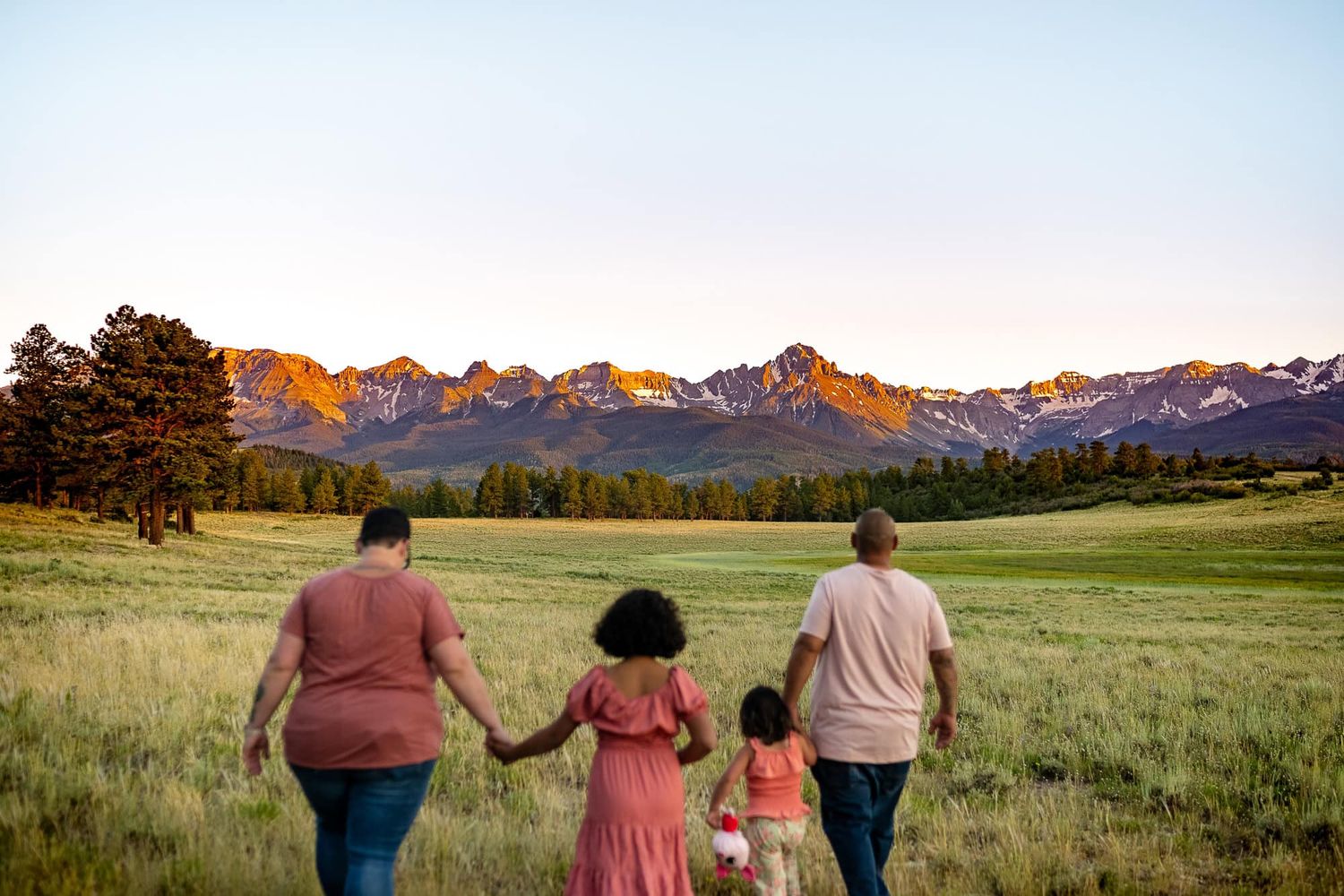 A family holds hands while walking towards mountain peaks during sunset.