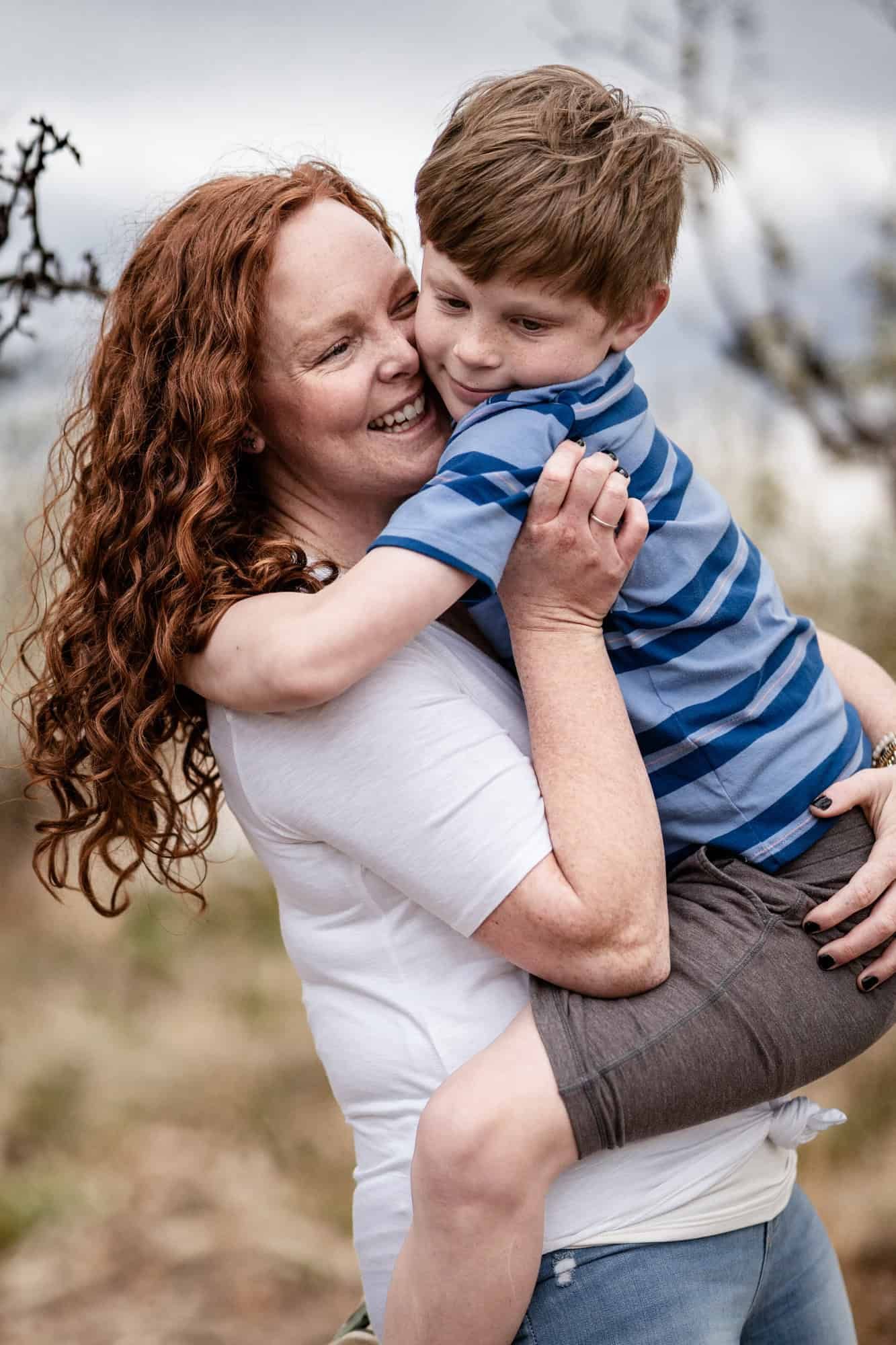 Parent holding and hugging young child wearing striped shirt outdoors.