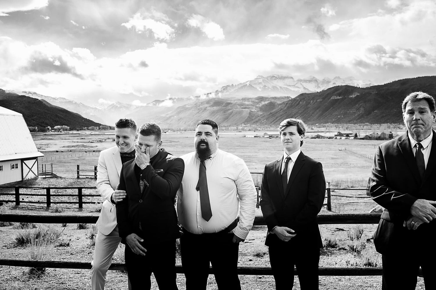 Groomsmen in formal attire pose together against a mountainous landscape backdrop.