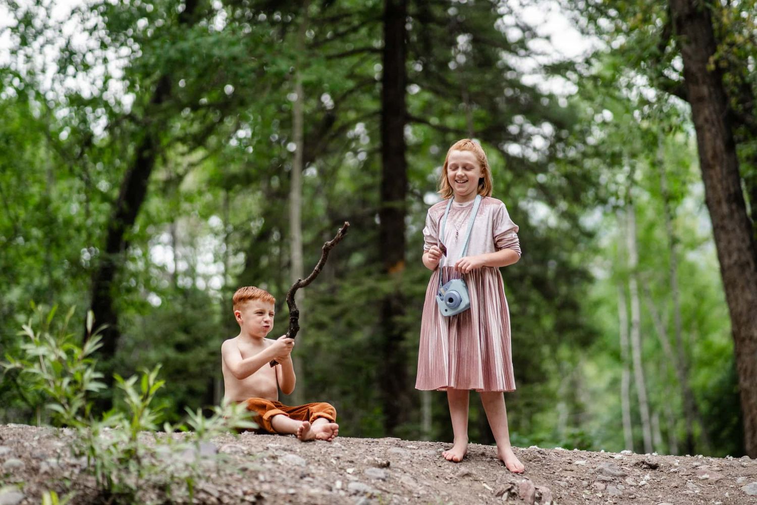 Two children relaxing on forest hillside during outdoor adventure.