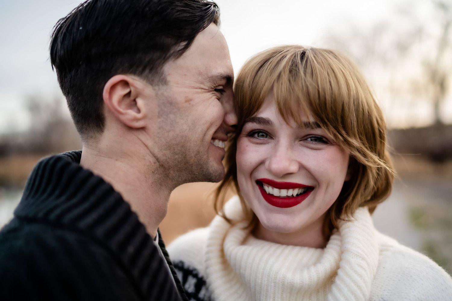 Joyful couple in winter sweaters share intimate laughter outdoors.