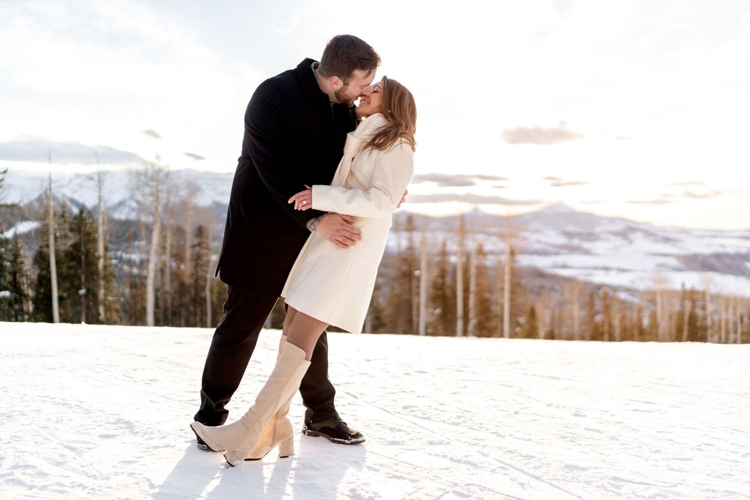 Romantic dip kiss pose in the snow with mountain scenery and winter attire.