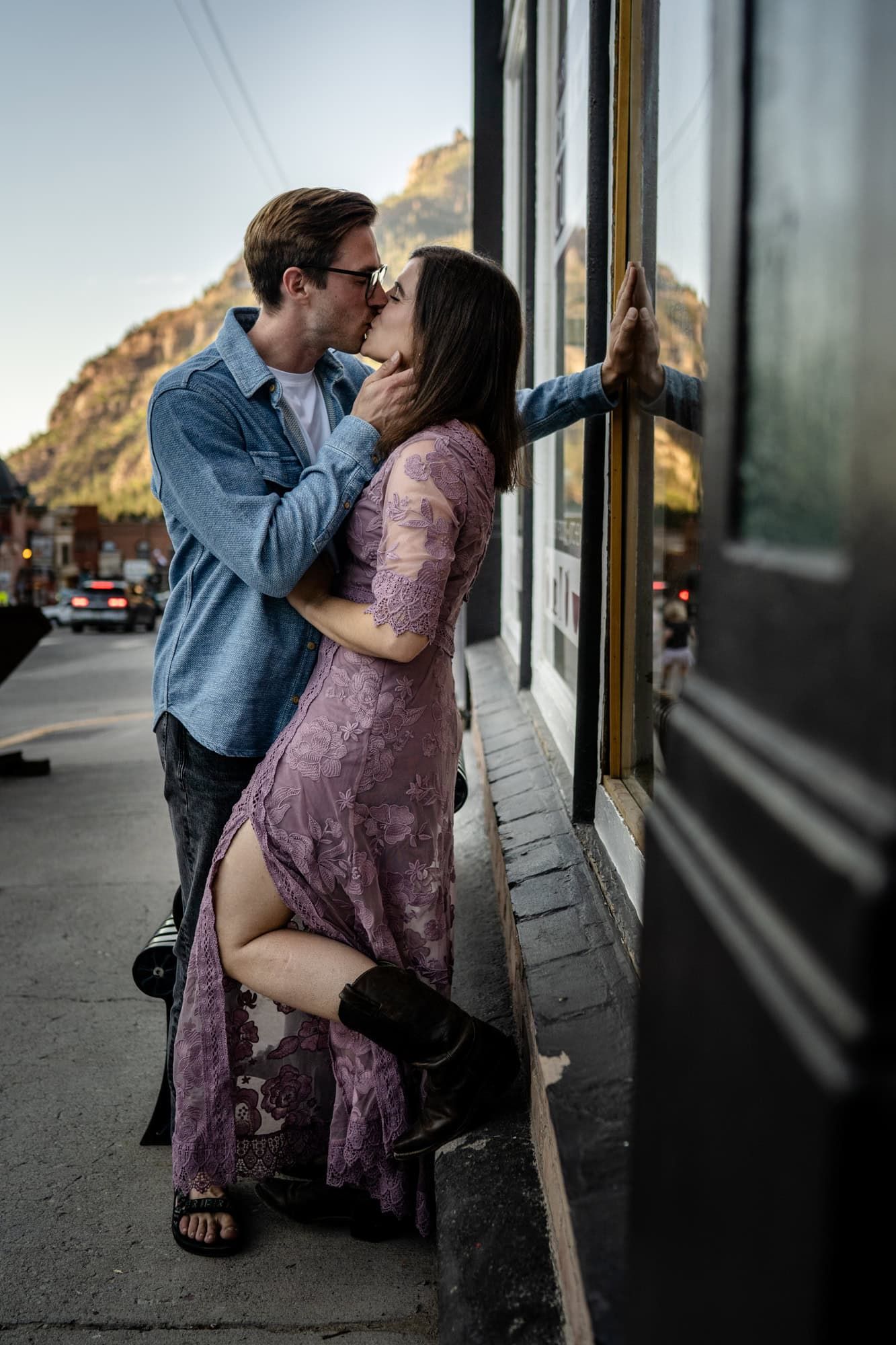 A romantic couple sharing an intimate moment against a storefront with mountains in the background.
