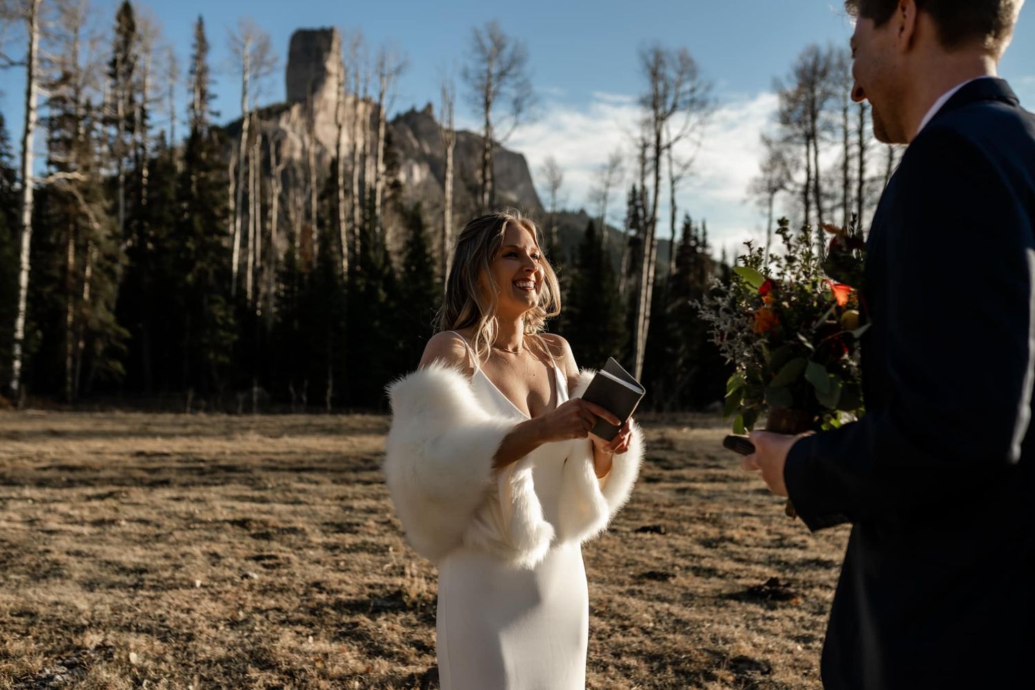 A winter wedding moment with snow-capped mountains and evergreen trees in the background.
