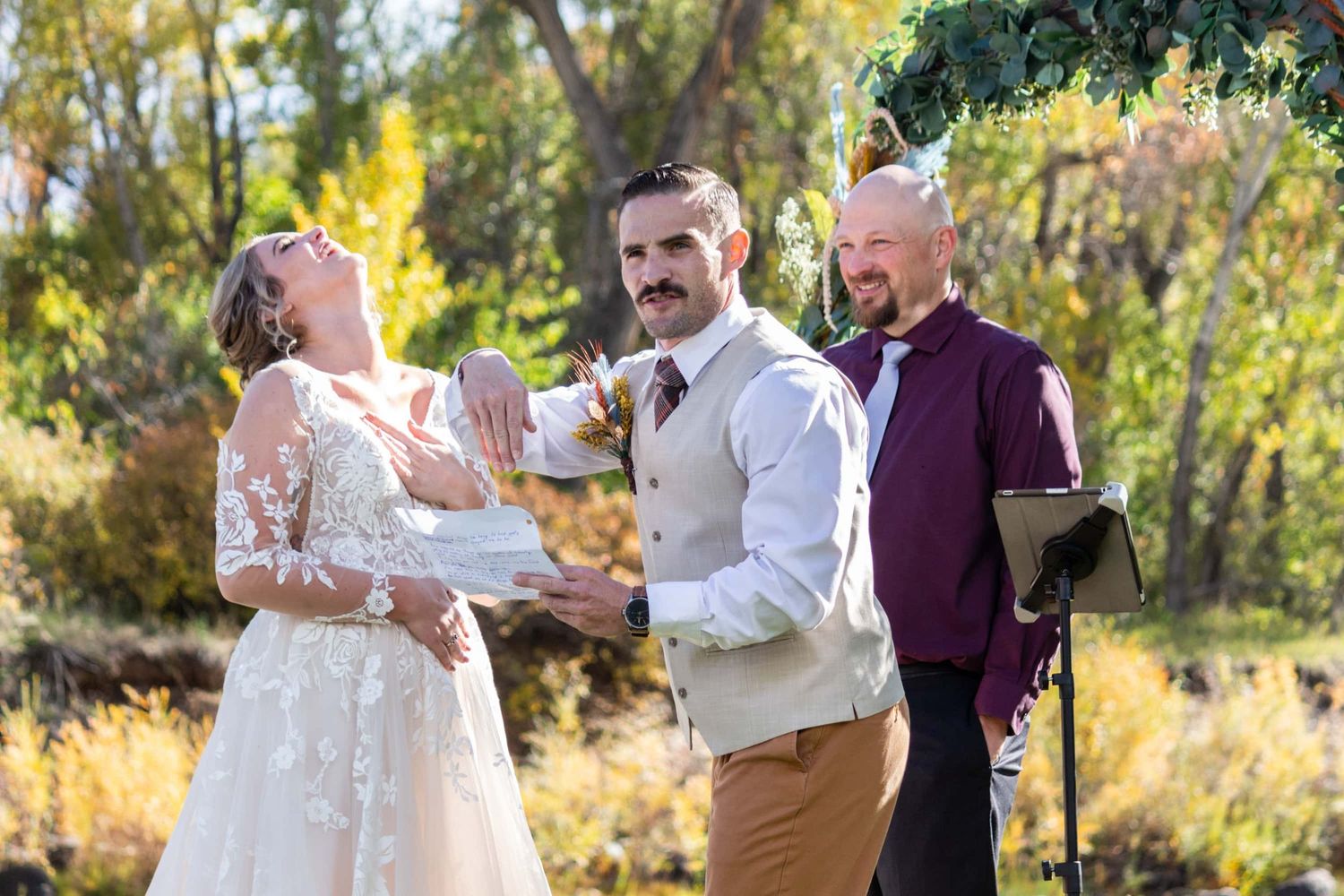 Wedding party laughing together during outdoor autumn ceremony.