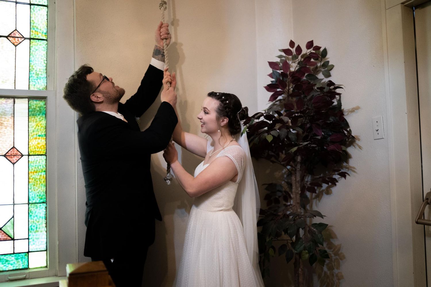 Playful moment between newlyweds inside church with stained glass windows.