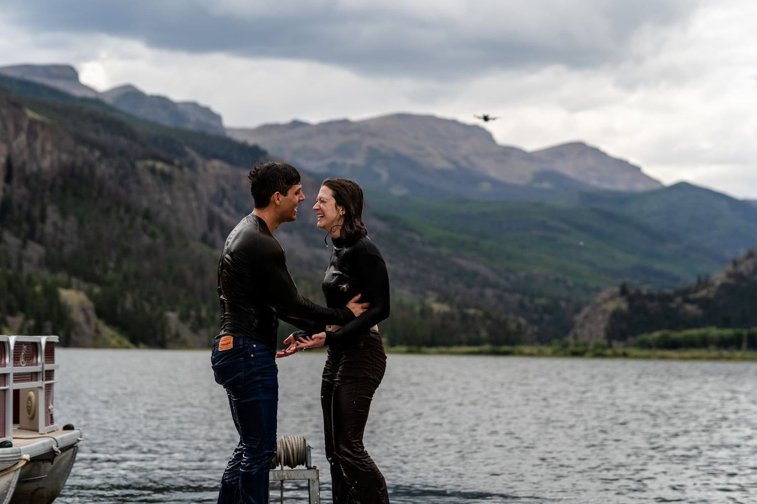 A tender moment shared between a couple on a dock with mountain scenery.