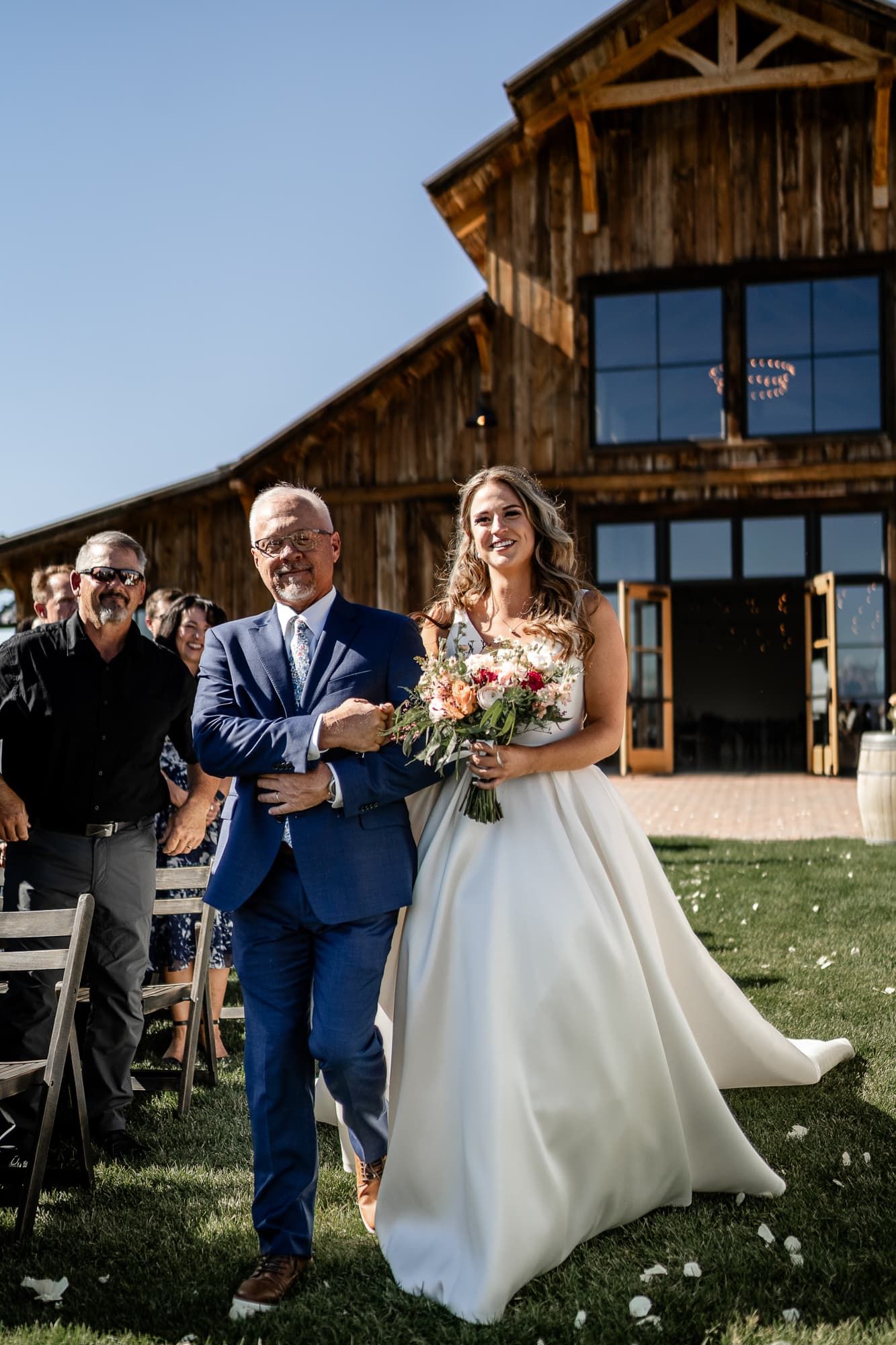 Father of bride walks her down the aisle at an outdoor wedding barn venue near Montrose Colorado.