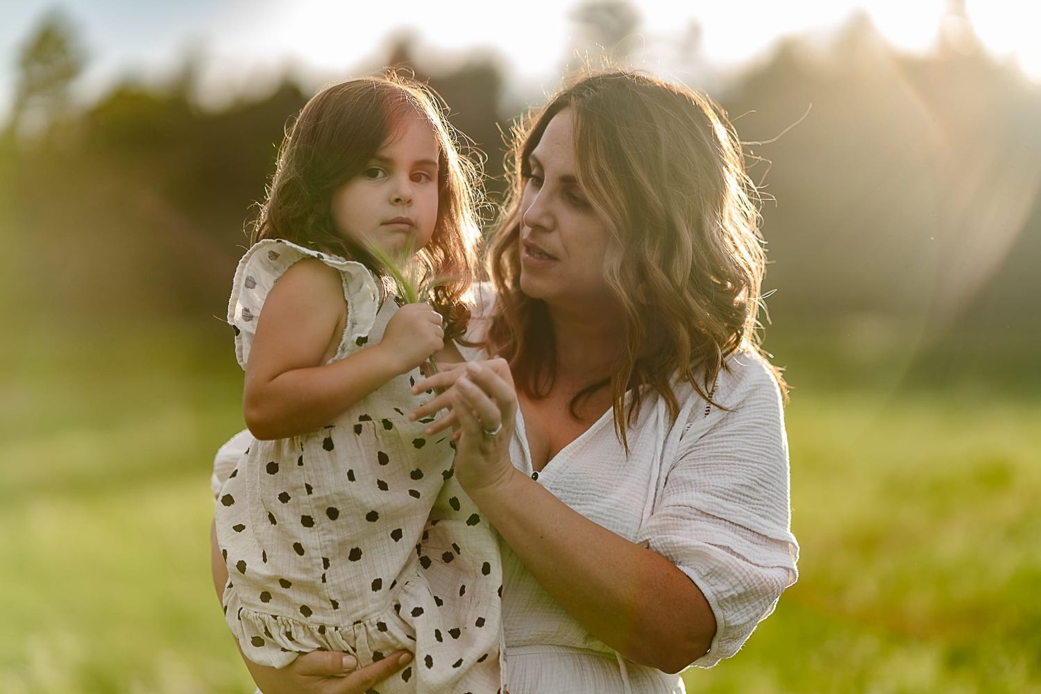 A parent and child share a tender moment in golden evening light outdoors.
