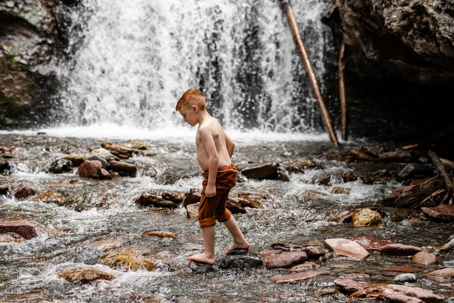 Child wading through rocky stream near cascading waterfall in nature.