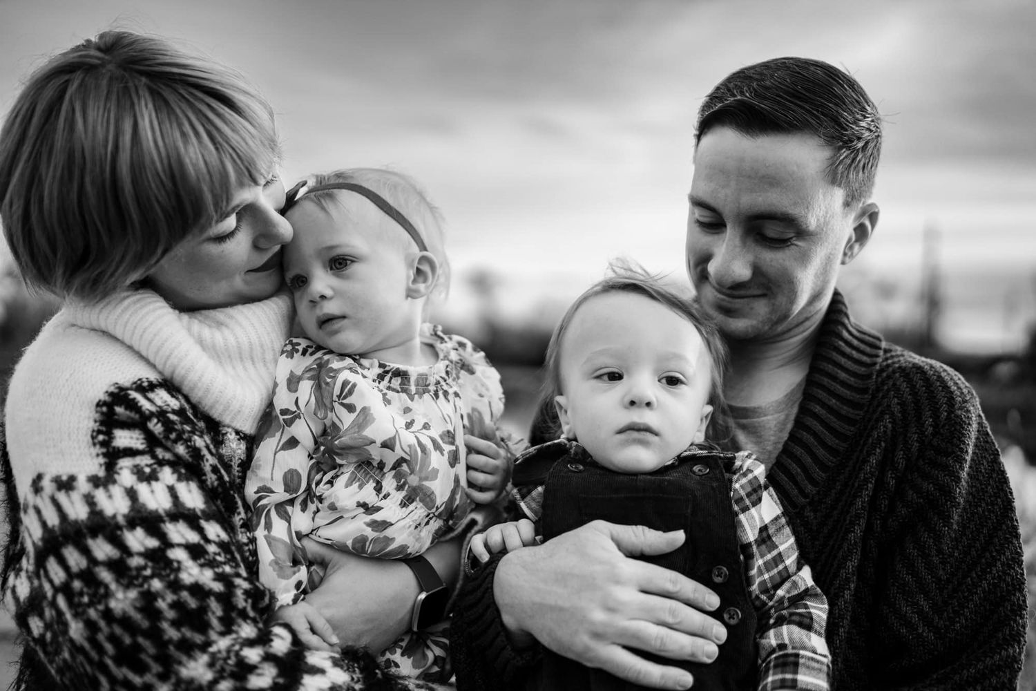 A family of four shares an intimate black and white portrait moment outdoors.