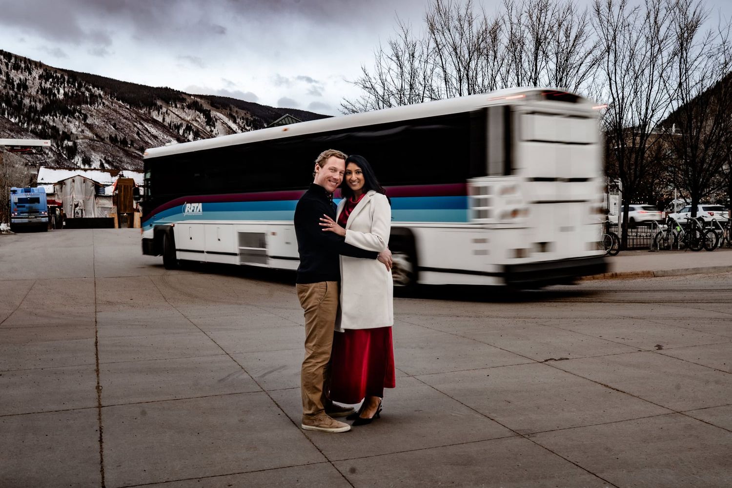 A couple embracing in front of a tour bus against a mountainous winter landscape.