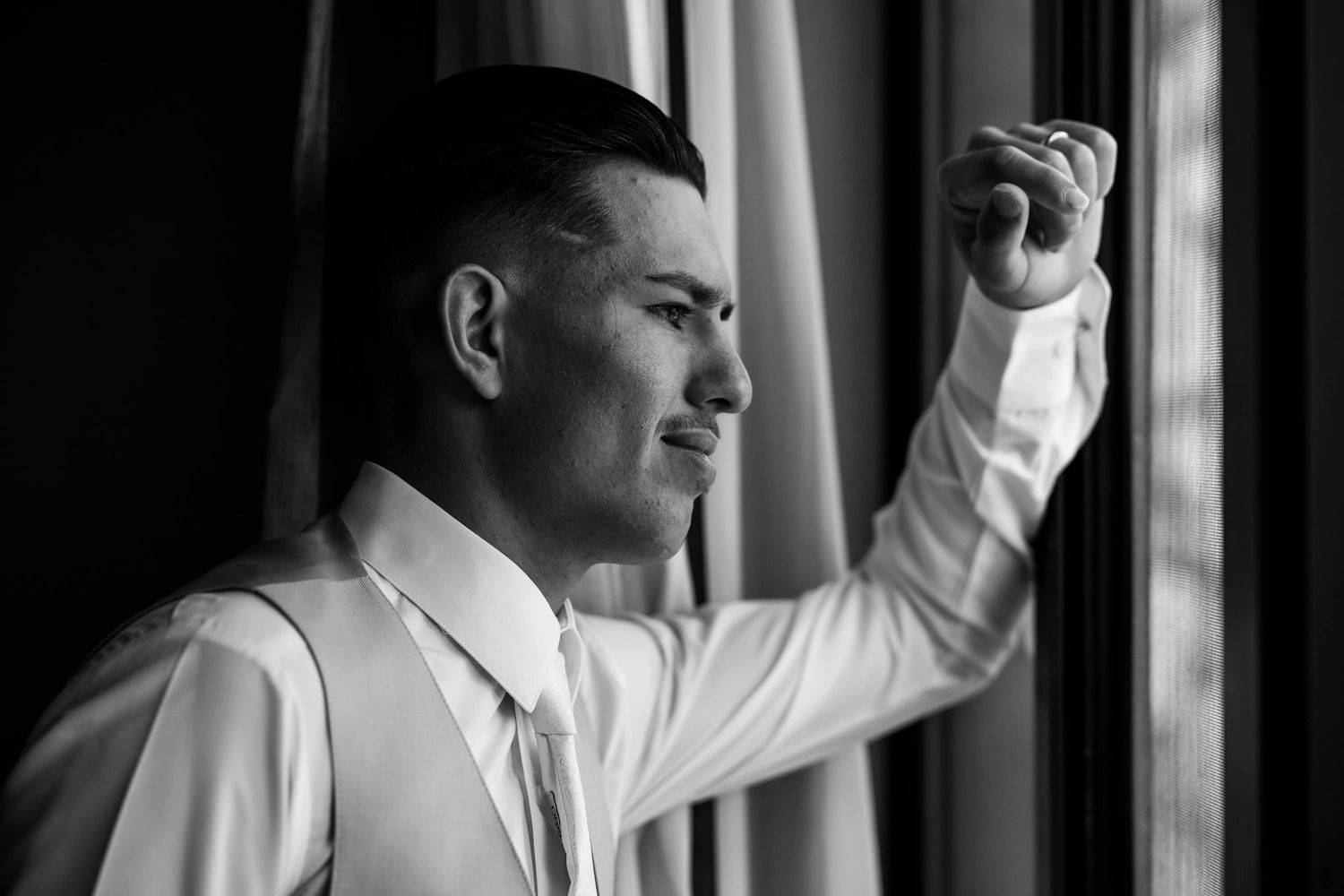 Profile view of person in white dress shirt raising their fist while standing near window in black and white photo.
