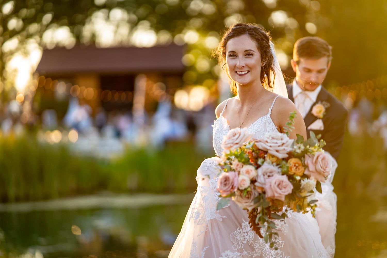 Groom holds bride's white lacey dress while they walk at golden hour. Captured by Montrose colorado wedding photographer