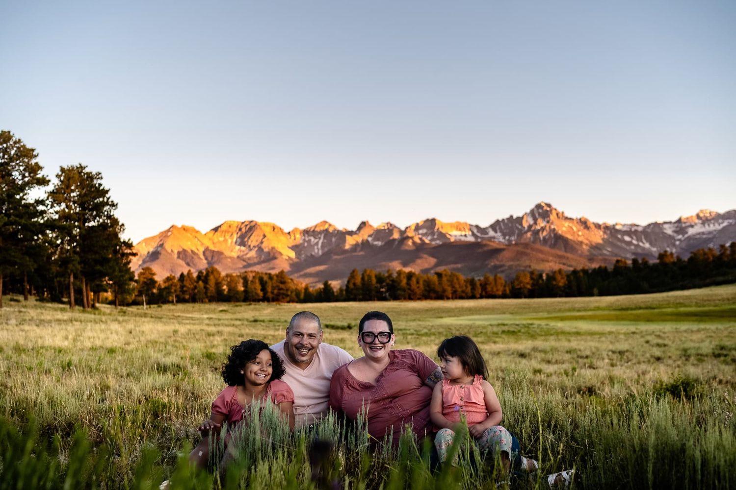 A family sits together in a mountain meadow during golden hour.
