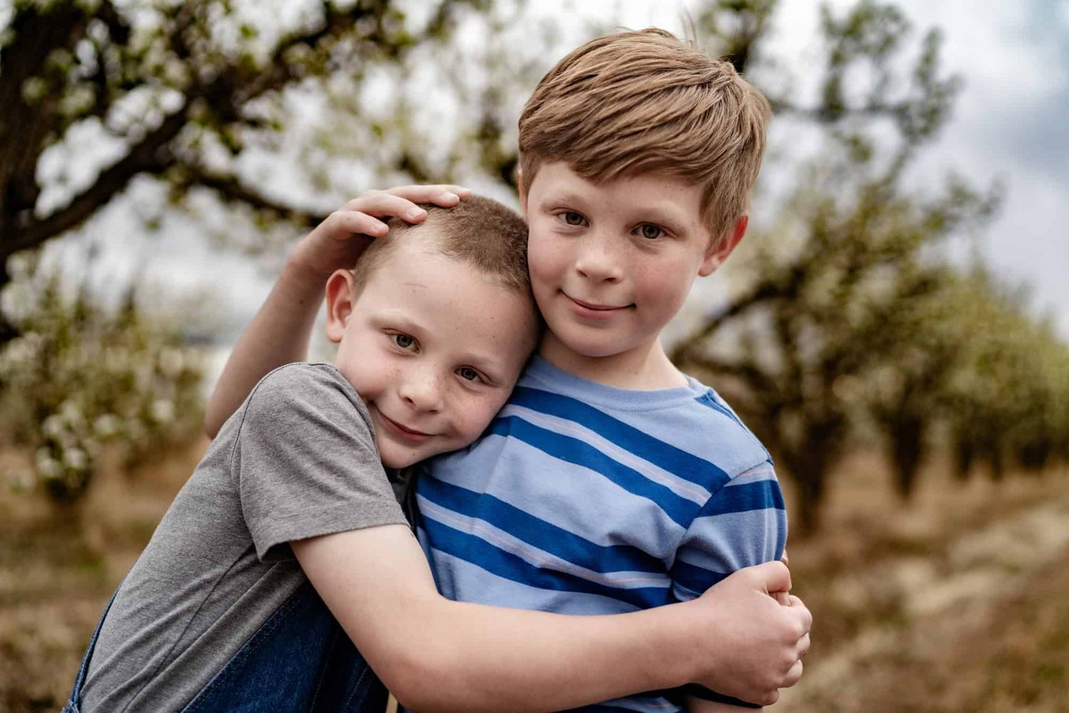 Two young boys hugging and smiling at camera in a rustic outdoor setting.