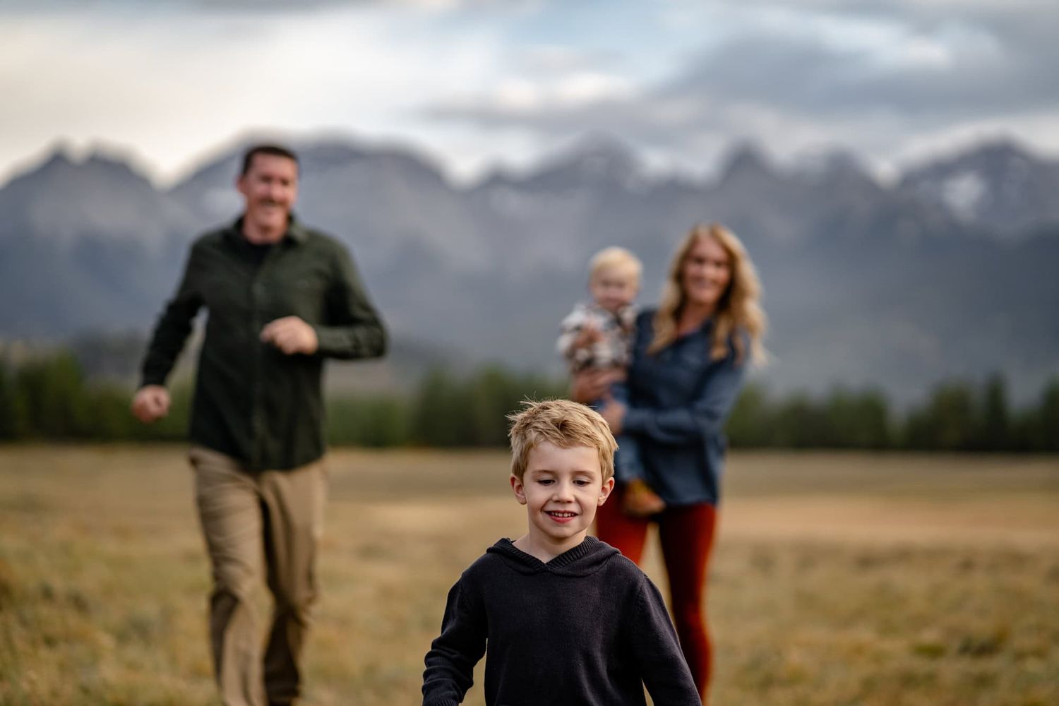 Family running and playing in a meadow with snow-capped mountains in the distance.