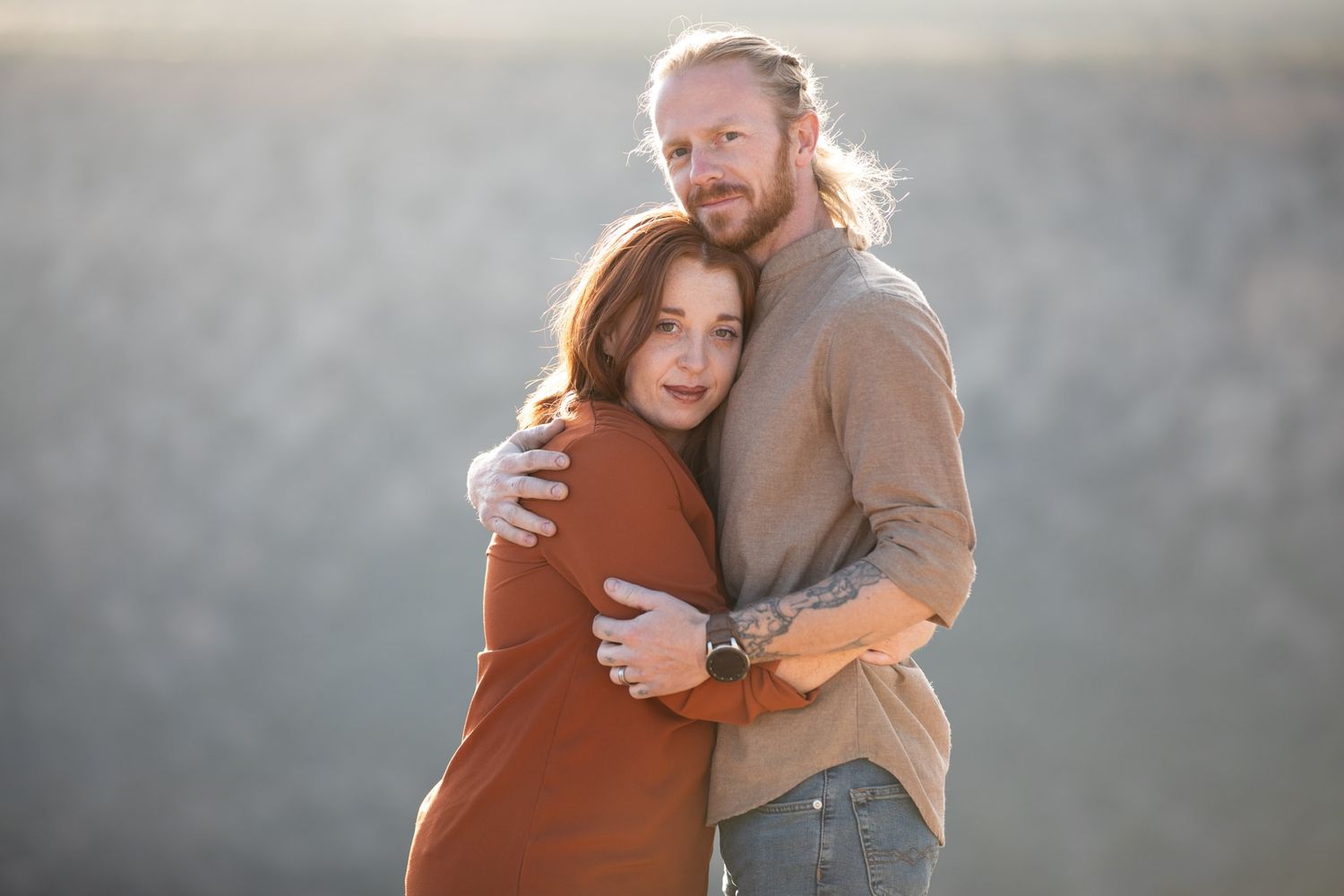A couple embraces in warm sunlight against a misty mountain backdrop.