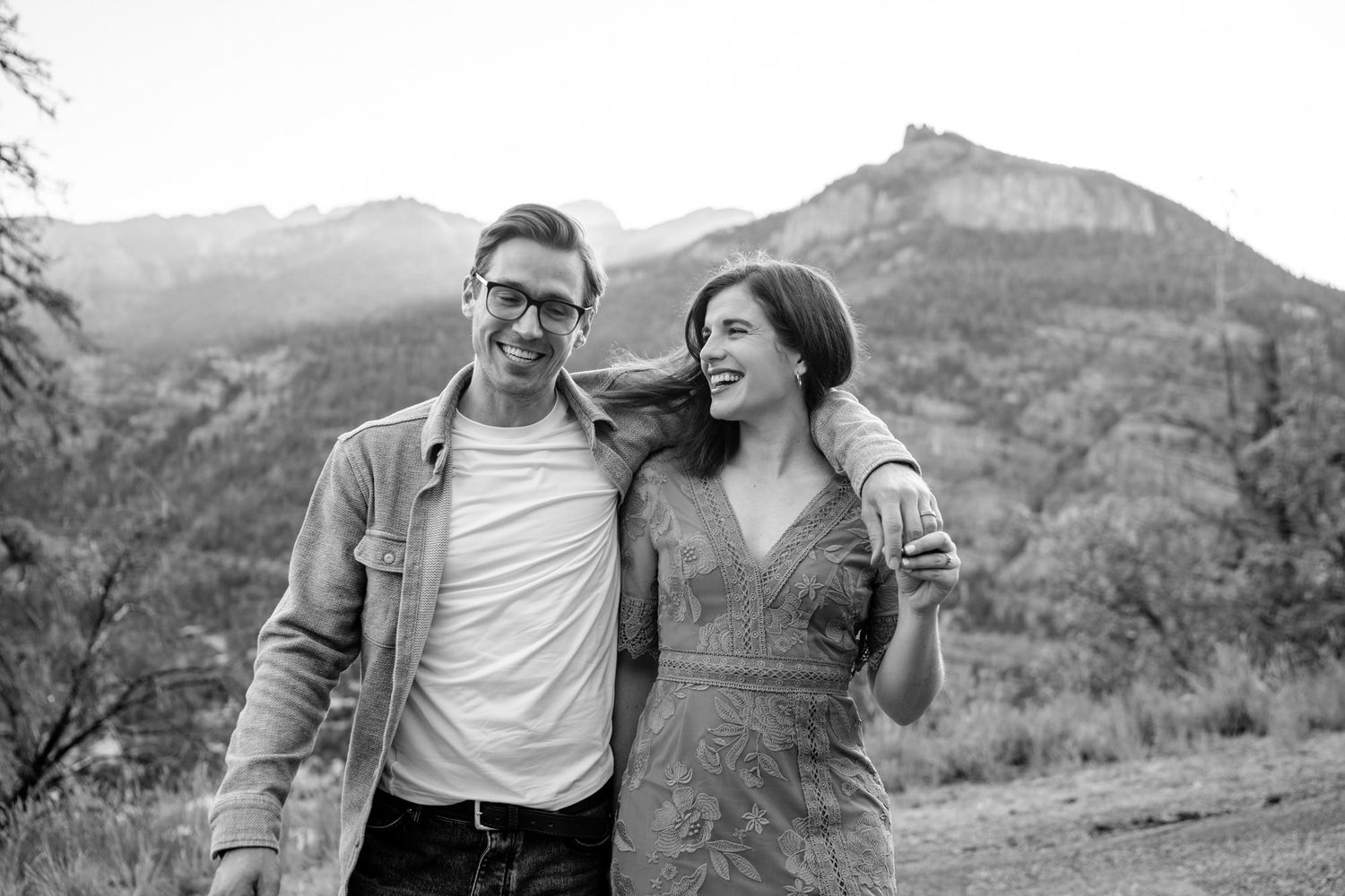 A couple laughs together while hiking in the mountains on a sunny day.