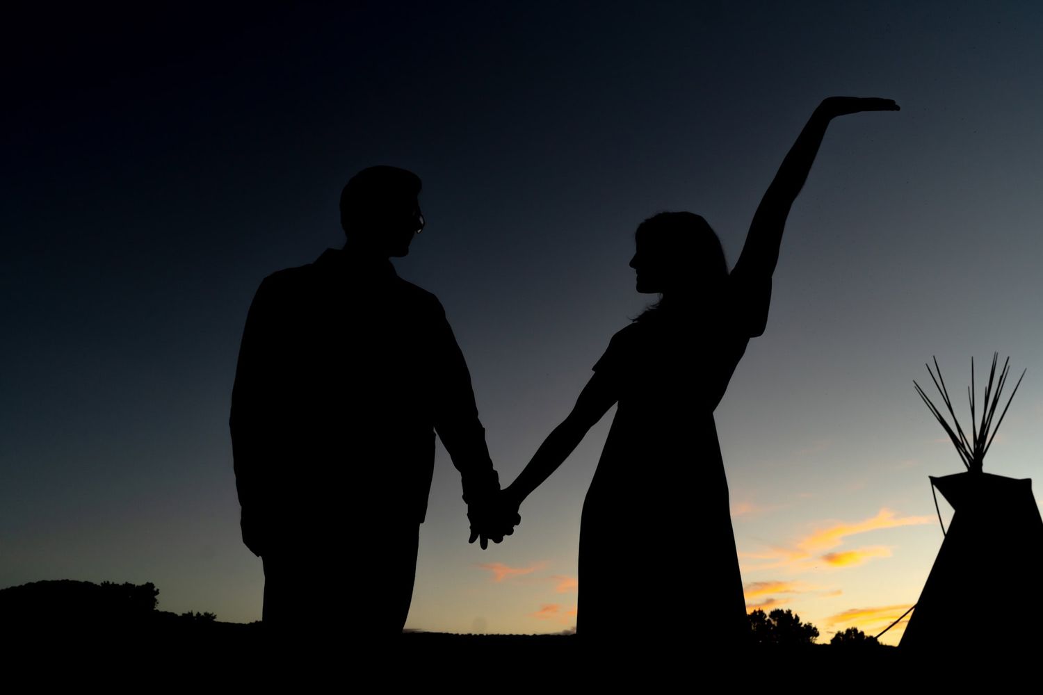 Silhouetted couple holding hands against a sunset sky with a woman's graceful pose.