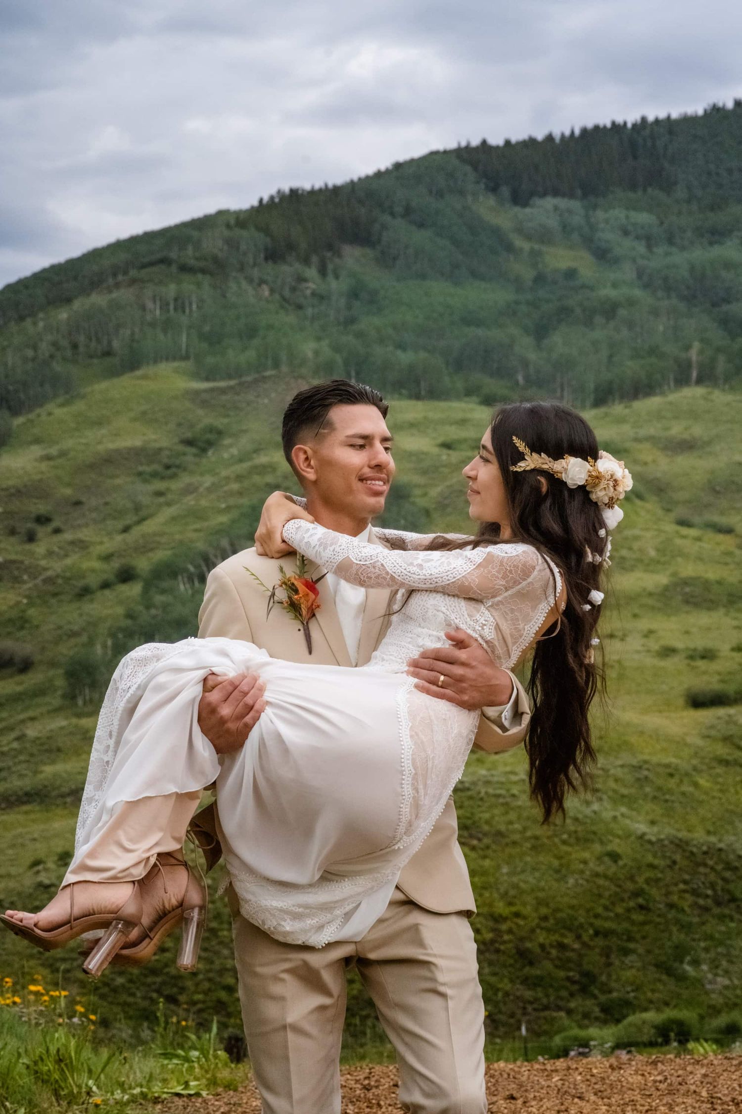 A romantic wedding scene with a couple embracing in front of lush green mountainside in a beautiful outdoor setting.