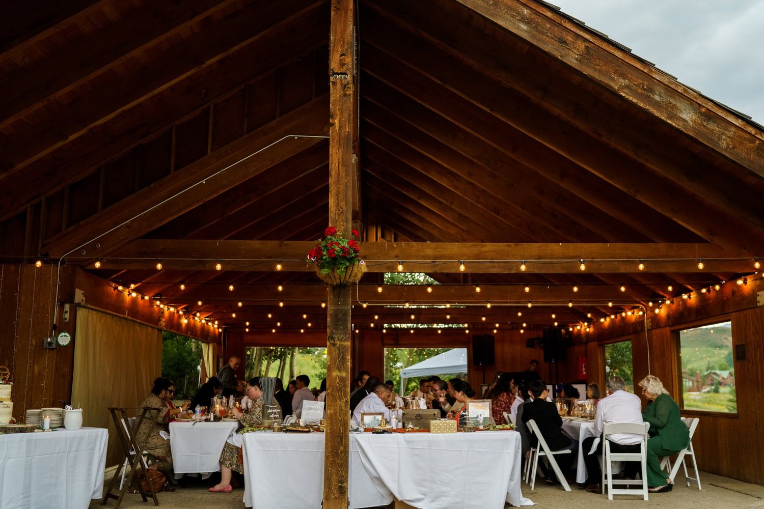 A rustic wooden barn venue decorated with string lights and white tables for a wedding reception.