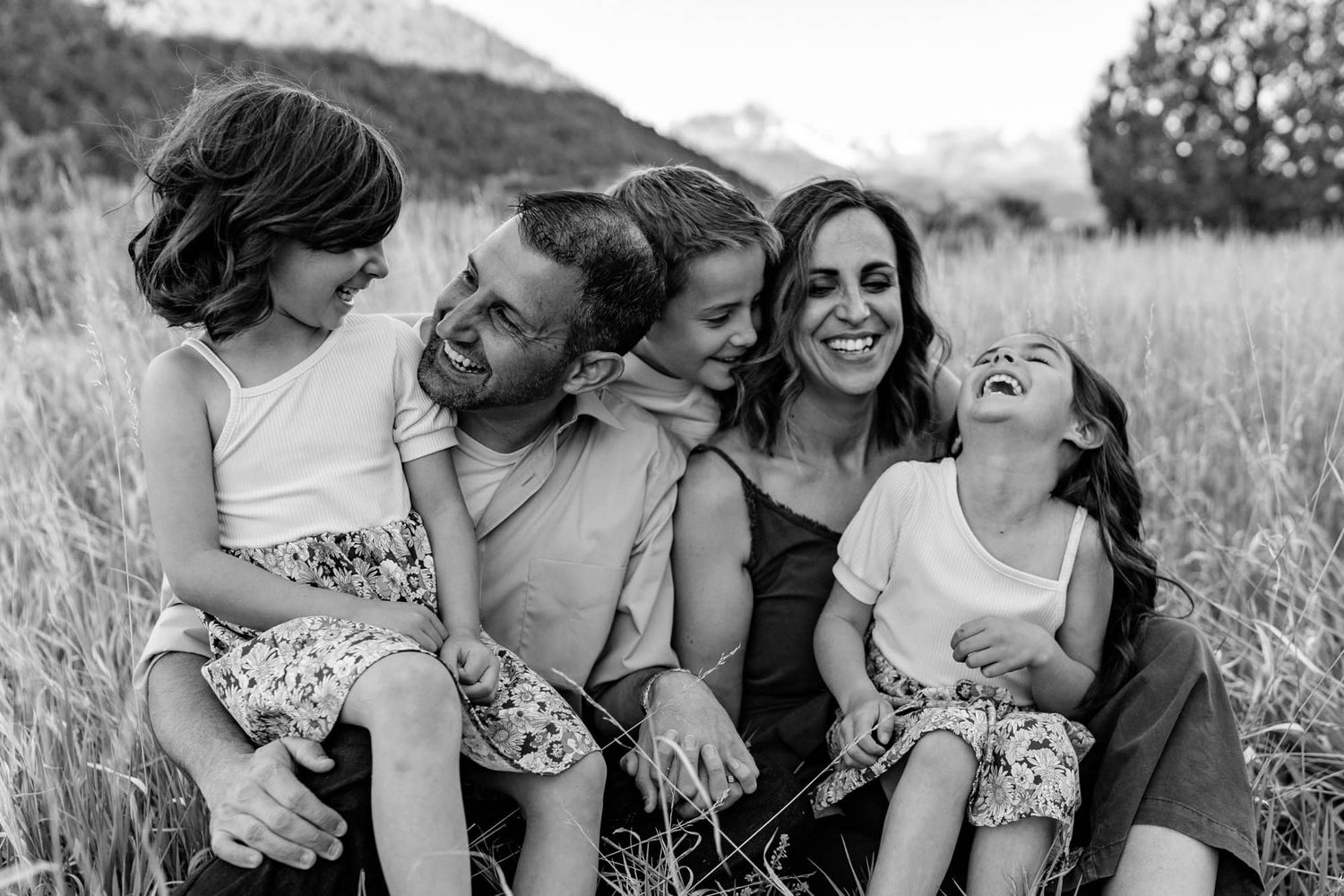 A candid black and white portrait of a family sharing laughter in a meadow.